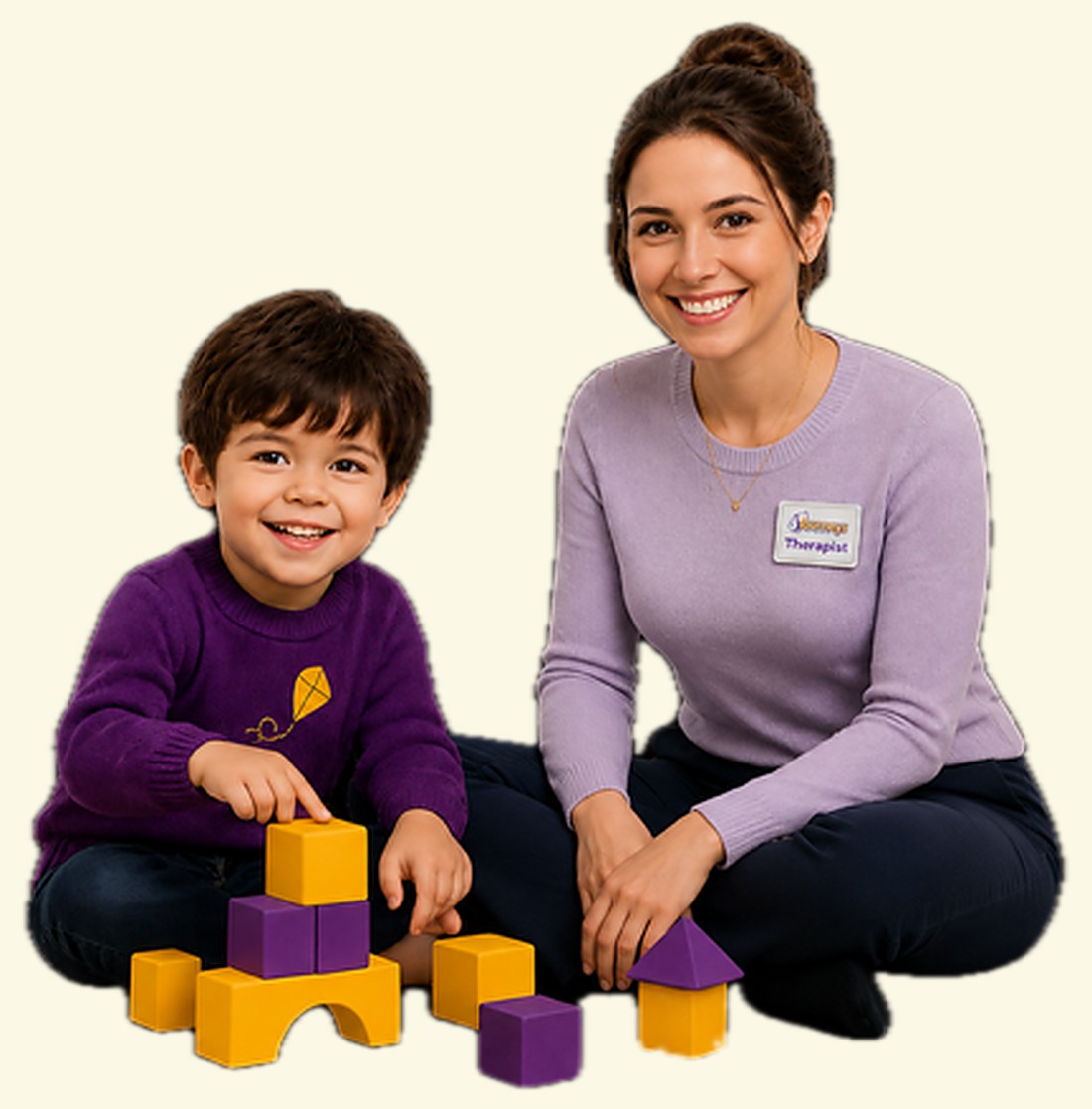 A Journeys ABA therapist and a young boy in a purple kite sweater smiling together beside a tower of purple and gold blocks
