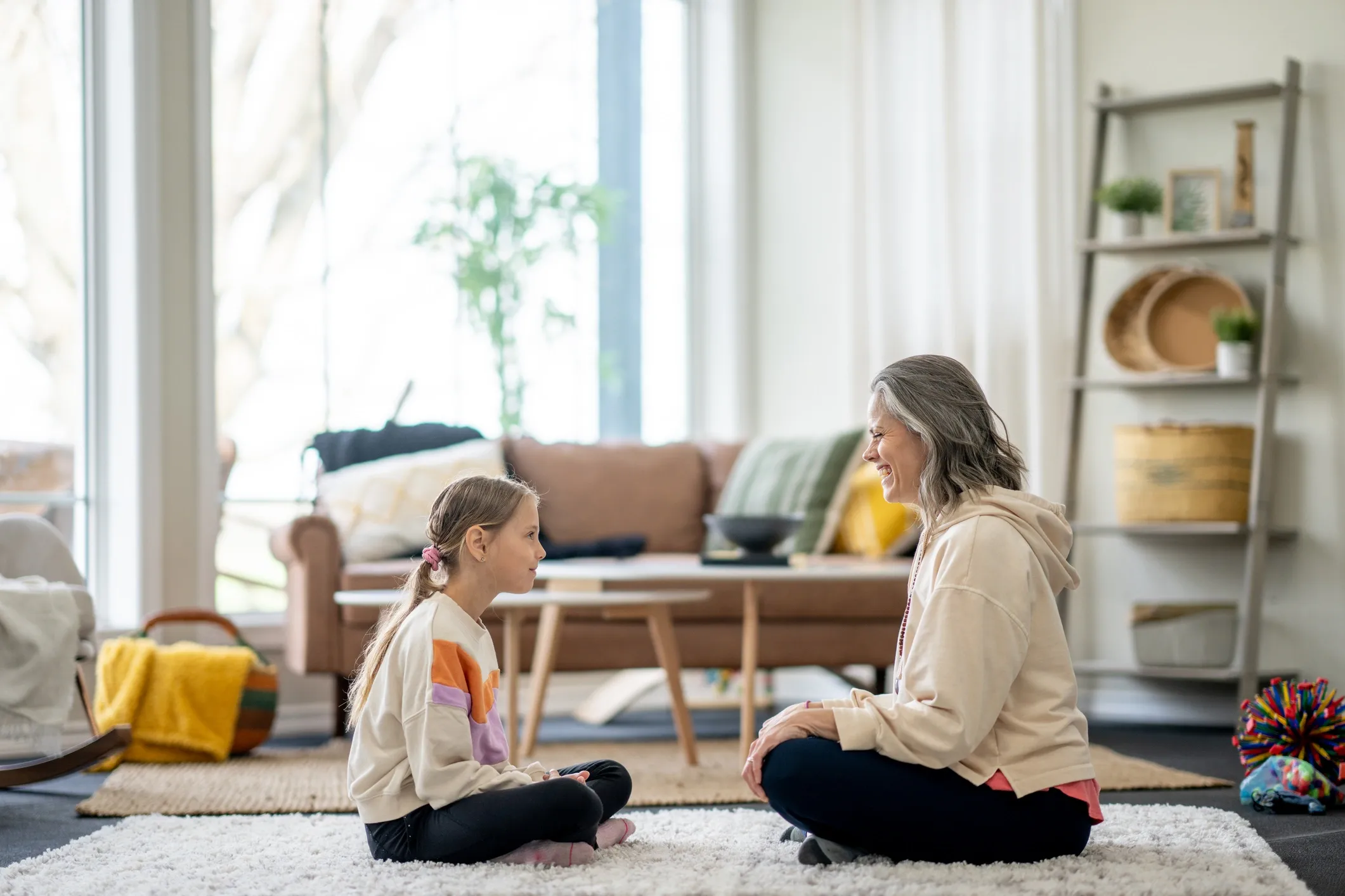 A child and her therapist sitting cross-legged on a living room rug during an in-home ABA session