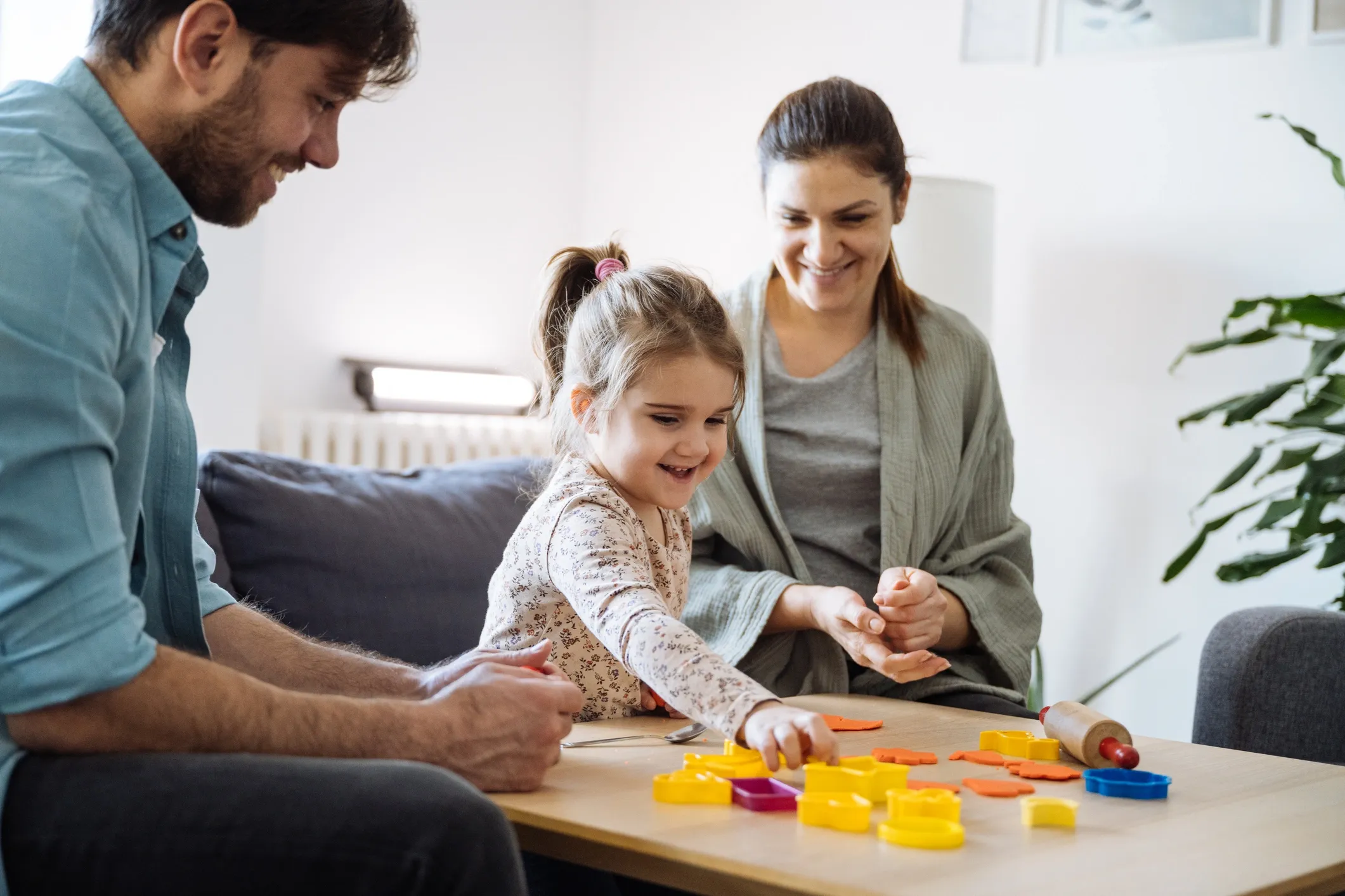 Parents playing with their young daughter at a table with colorful play-dough shapes